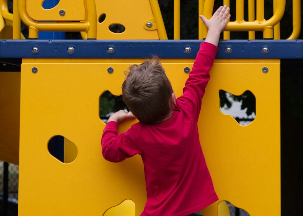 A young boy climbing up a yellow playground structure