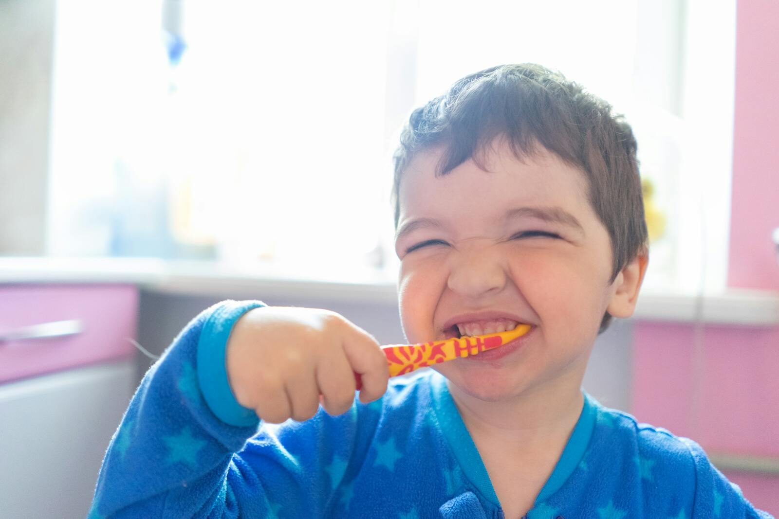 A young boy brushes his teeth while smiling
